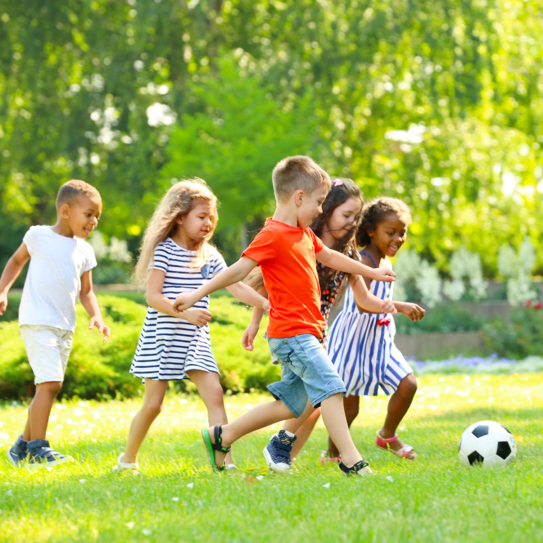 crianças em área verde de um parque correndo atrás de uma bola de futebol